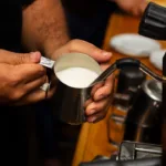 Barista schäumt Milch mit einer Dampflanze auf
